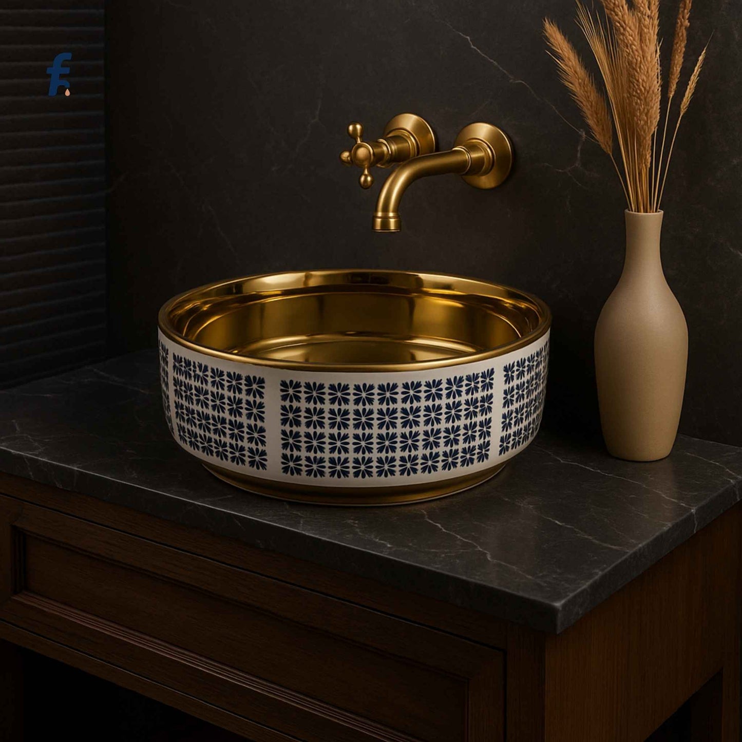 Gold sink with decorative pattern on a dark countertop, next to a beige vase with dried plants.