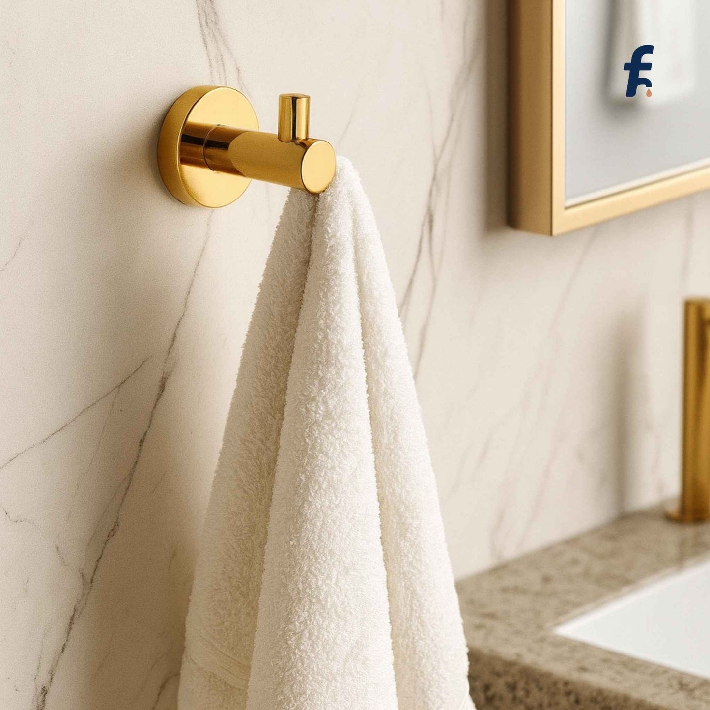 Gold towel hook with a white towel on a marble wall in a bathroom. Modern gold robe hook installed on marble wall in bathroom
