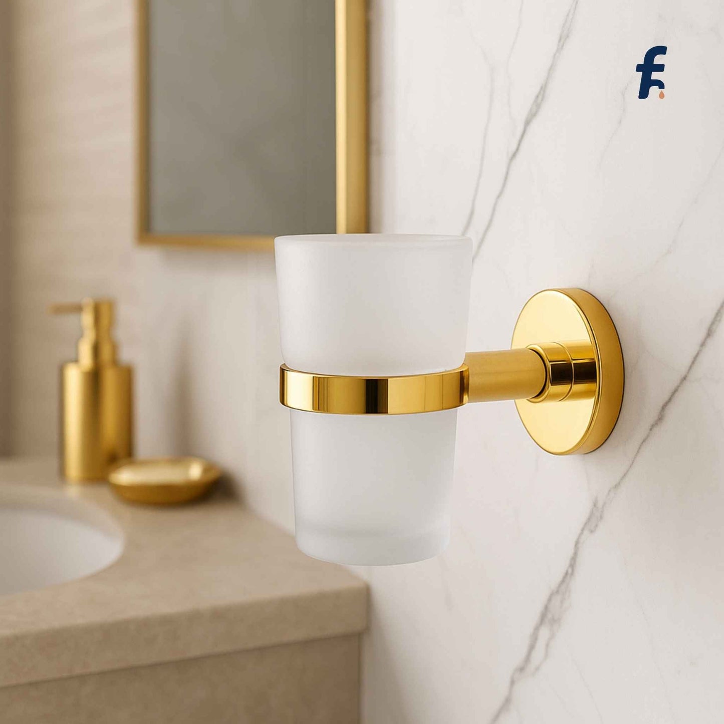 Gold wall-mounted glass holder on a bathroom wall with a mirror and sink in the background. Modern bathroom tumbler holder in gold finish with glass cup