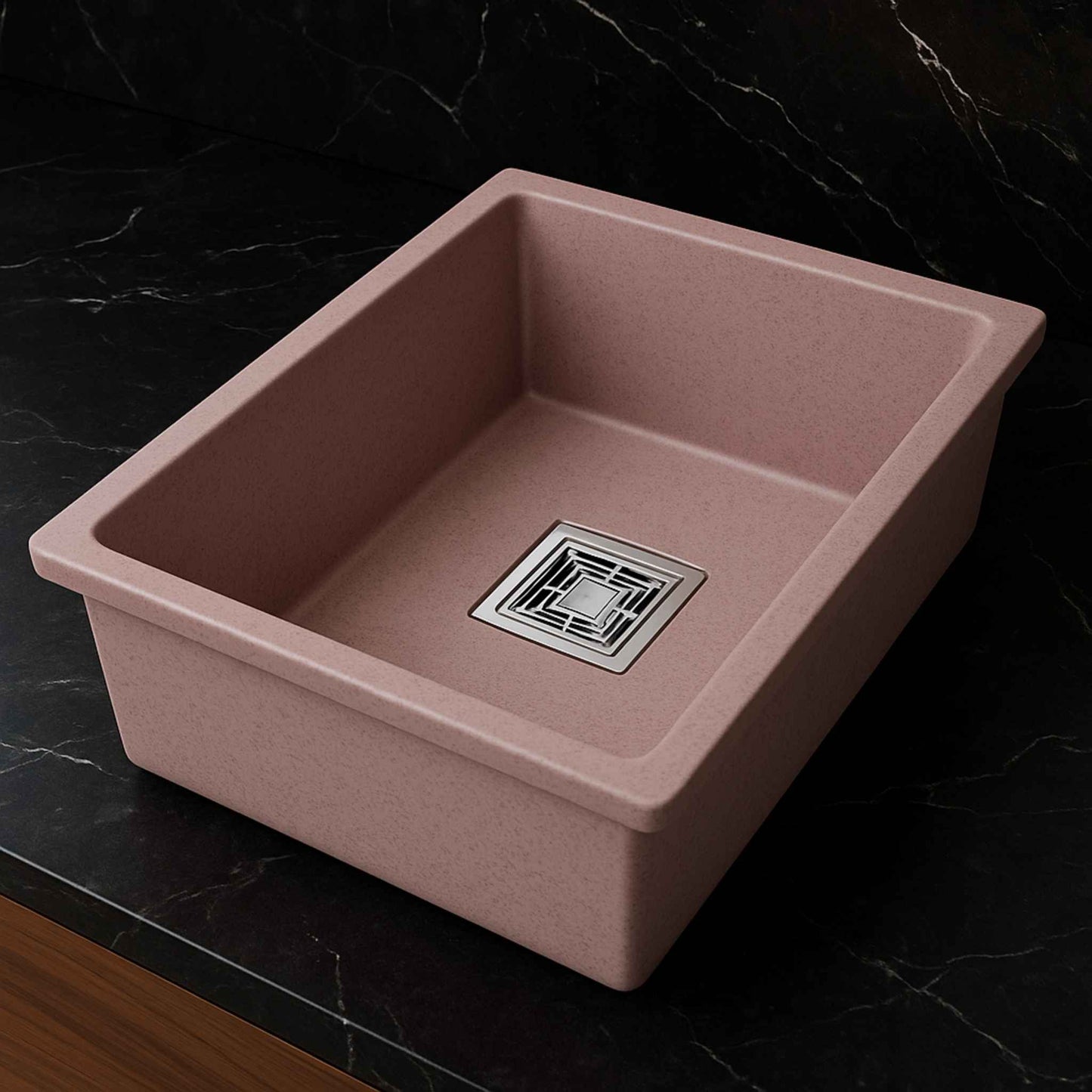 Side angle of rose pink kitchen sink placed in a dark marble countertop with brushed steel faucet