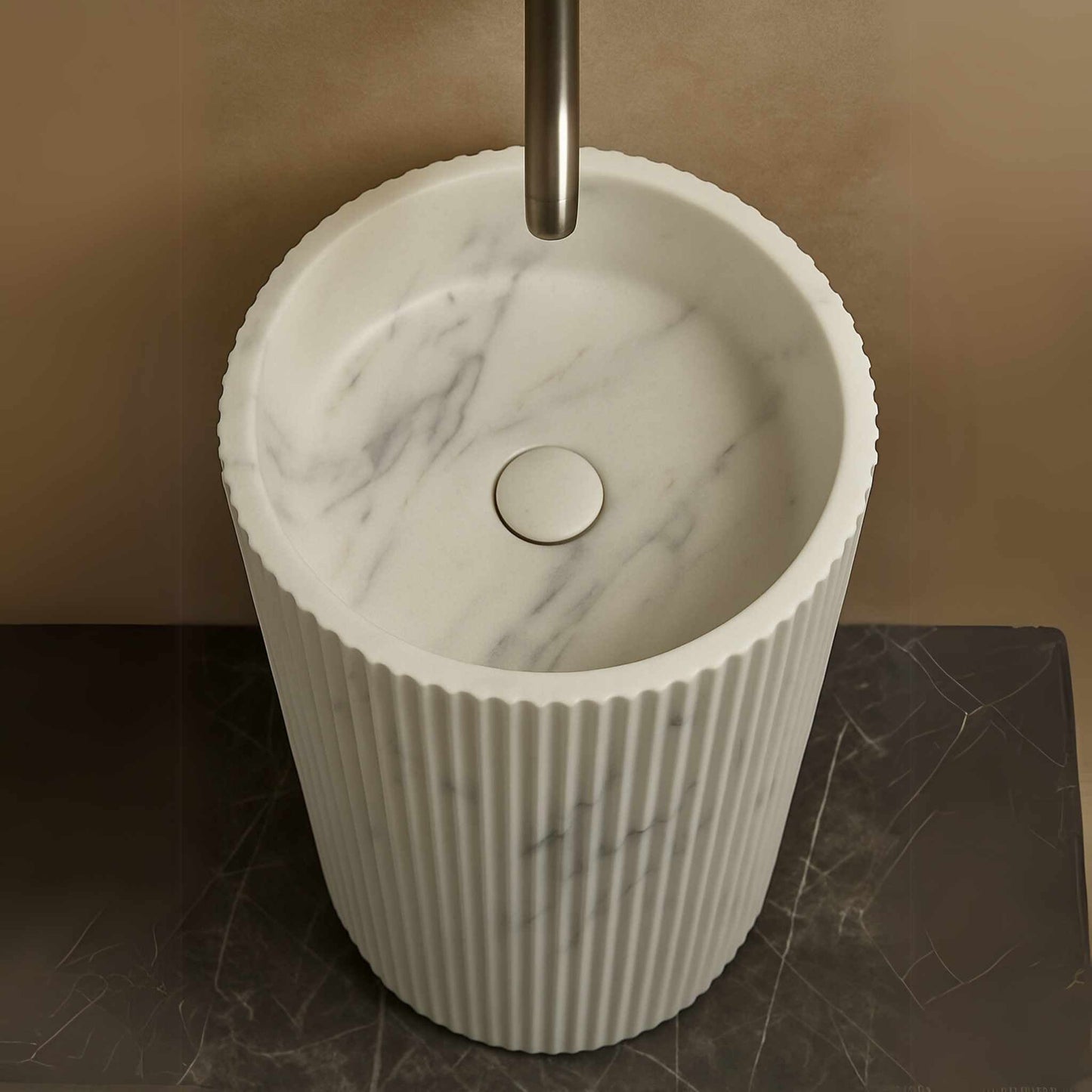 Top-down view of round white marble basin with fluted edges and silver faucet