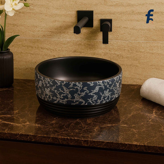 Front view of EQTT-515 glossy black round wash basin with intricate floral design, placed in a luxurious marble bathroom setup with gold wall-mounted faucet.