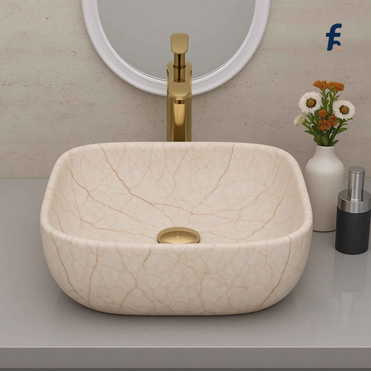 Beige ceramic sink with gold faucet on a bathroom counter, featuring a mirror and decorative elements. 