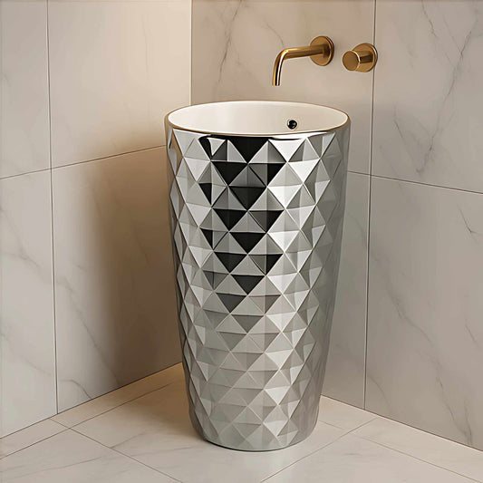 Diamond cut silver pedestal wash basin with glossy texture and white round top, styled with a gold wall-mounted tap in a modern luxury bathroom.