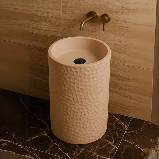Pebble-textured pedestal washbasin in luxury bathroom with marble floor and brass faucet