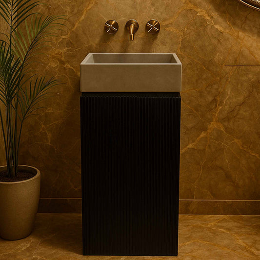  Front view of a luxury black fluted pedestal washbasin with grey concrete basin and wall-mounted brass faucet in a marble bathroom.