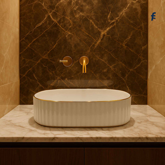 White ceramic sink with gold fixtures against a marble wall.