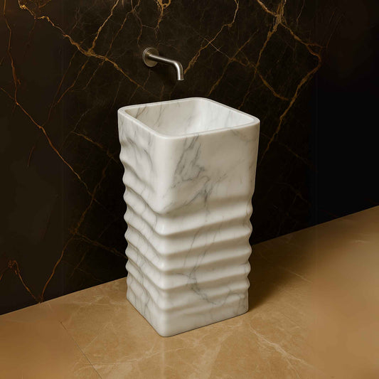 Sculptural white marble pedestal sink placed in a luxurious bathroom with gold-veined tiles