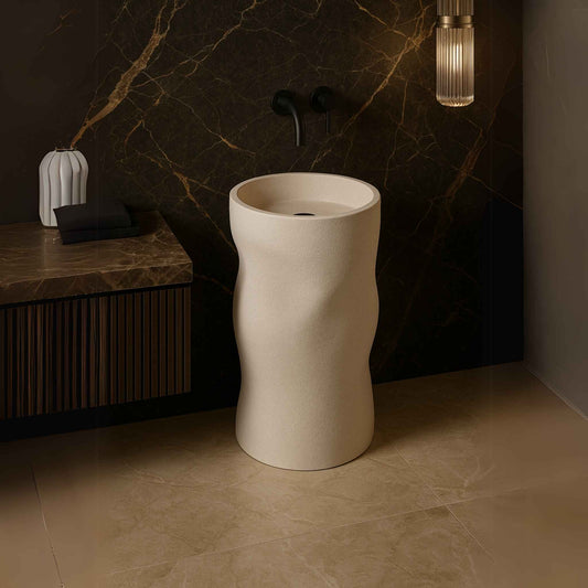 Luxury sculpted pedestal washbasin in matte ivory finish with wall-mounted black faucet placed in a high-end bathroom setting