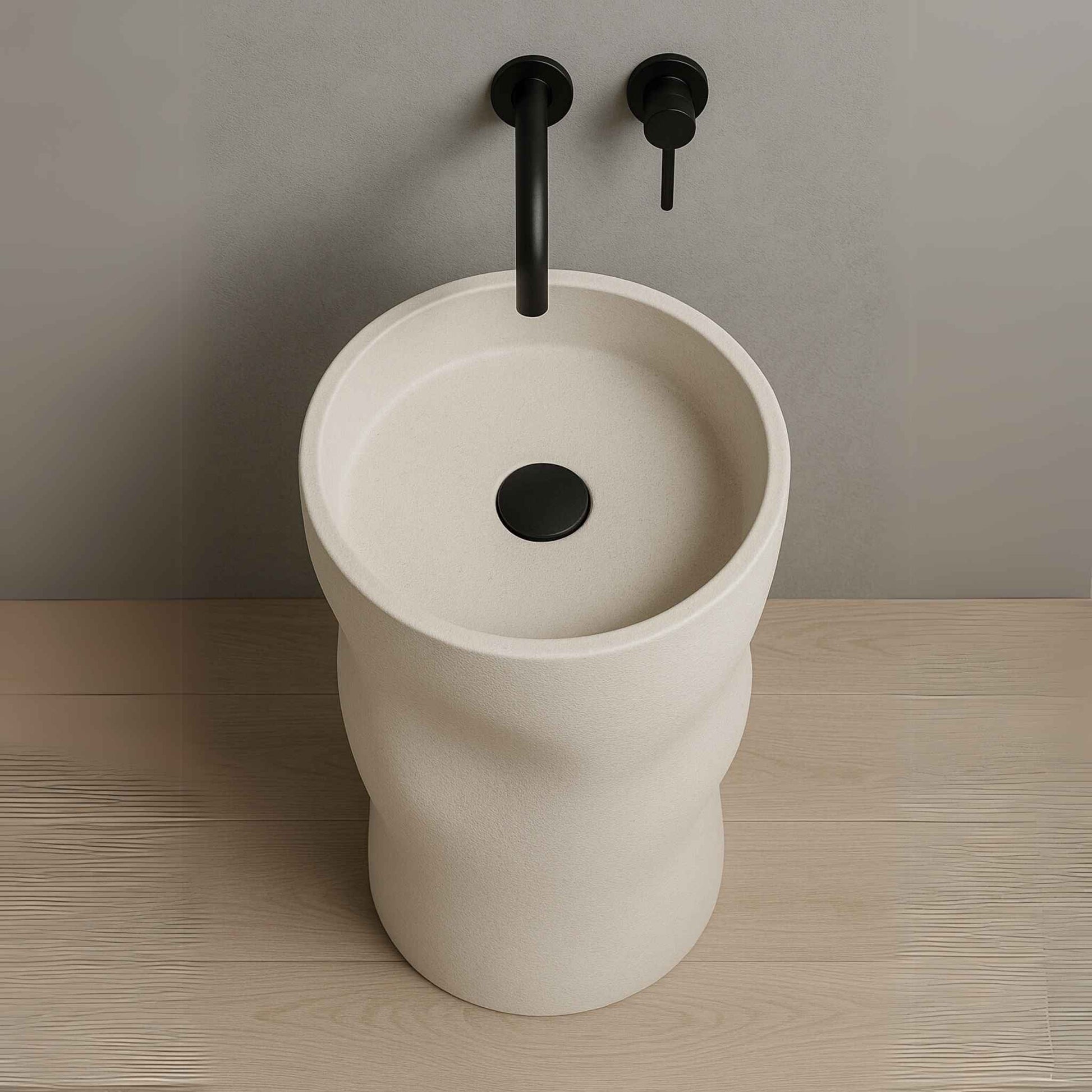 Luxury sculpted pedestal washbasin in matte ivory finish with wall-mounted black faucet placed in a high-end bathroom setting top angle