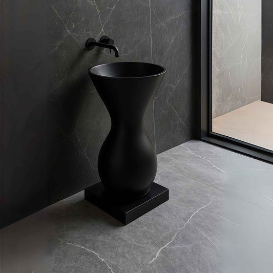 Matte black pedestal washbasin styled in an Italian marble bathroom with wall-mounted faucet, luxury setup.