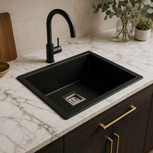 Matte black kitchen sink installed in marble countertop with black faucet and gold cabinet handles