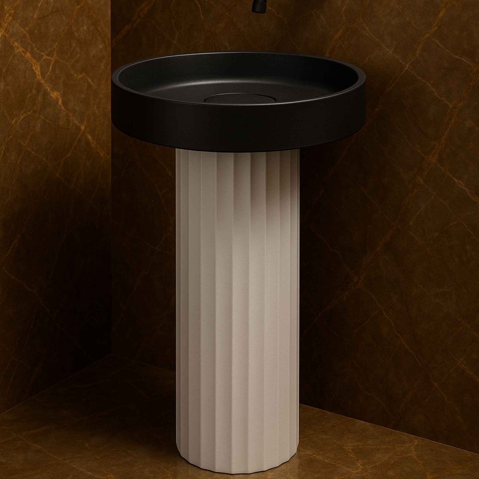 Side angle of modern round pedestal washbasin featuring black basin and fluted white cylindrical base placed against warm marble walls.