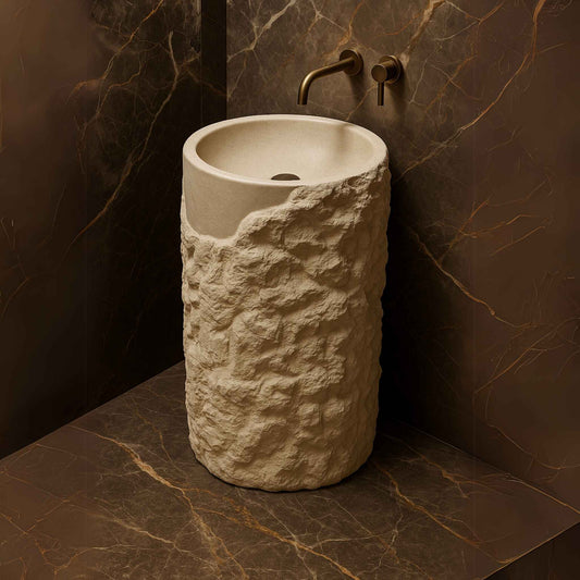 Luxury freestanding stone pedestal washbasin with rugged texture and brass wall faucet in a marble bathroom top angle
