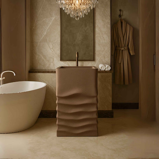 Front view of a taupe textured pedestal washbasin placed in a luxurious marble bathroom with a crystal chandelier and elegant bronze faucet.